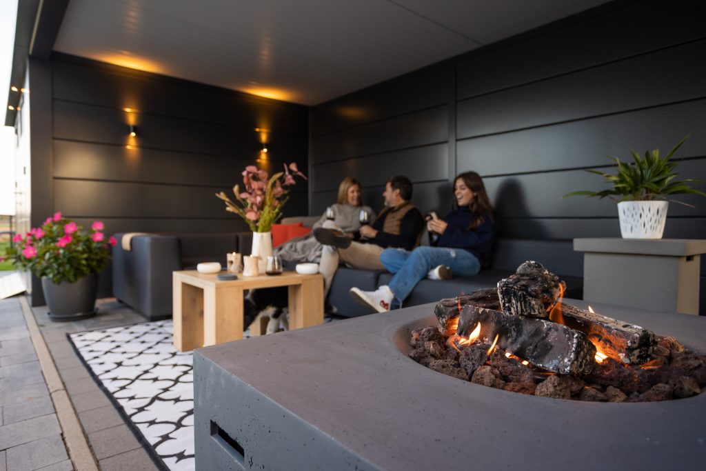 A wider shot Photo looking into the lounge with a family enjoying a gas fire pit in the Eleganto Lounge 3330 with Extra Large Lounge in Anthracite with Optional Windows